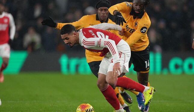 DUEL SENGIT: William Saliba berebut bola dengan Tolu Arokodare dalam laga Premier League antara Wolverhampton vs Arsenal di Molineux Stadium pada Kamis (19/2/2026). (Foto: (c) AP Photo/Dave Shopland)