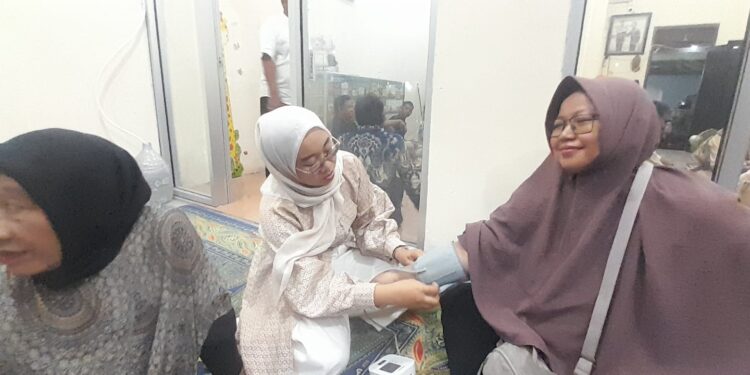 CEK KESEHATAN: Apoteker Alifia Maya Fatmawati (tengah) mengecek tekanan darah salah seorang peserta bakti sosial cek gula darah gratis dalam rangkaian grand opening Apotek GWS Farma di Jalan Raden Fatah, Parung Serab, Ciledug, Kota Tangerang, Banten pada Minggu (31/5/2026) malam. (FOTO: UNSIYAH SANGIDAH/KORANINDOPOS.COM)